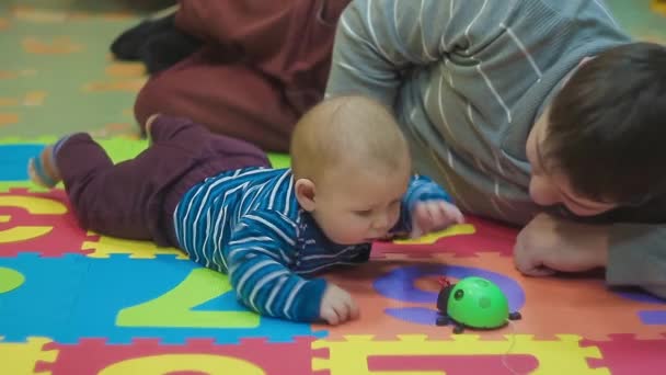 Peuter in trui is spelen met zijn vader speelgoed in de vorm van een lieveheersbeestje — Stockvideo