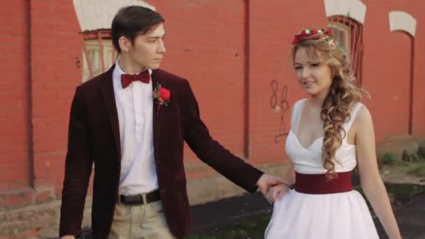 Novia y novio caminando a lo largo de una pared roja de ladrillo — Vídeos de Stock