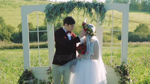 Невеста и жених держатся за руки возле свадебной арки — стоковое видео