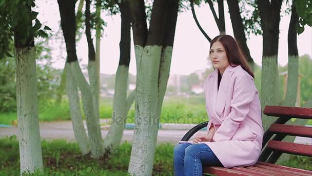 Κατεψυγμένα κορίτσι που κάθεται στον πάγκο σε ένα πάρκο φθινόπωρο — Αρχείο Βίντεο