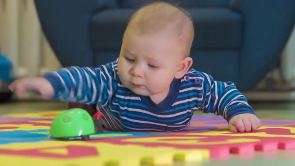 Il bambino sta giocando con il giocattolo sul tappeto a colori in camera — Video Stock