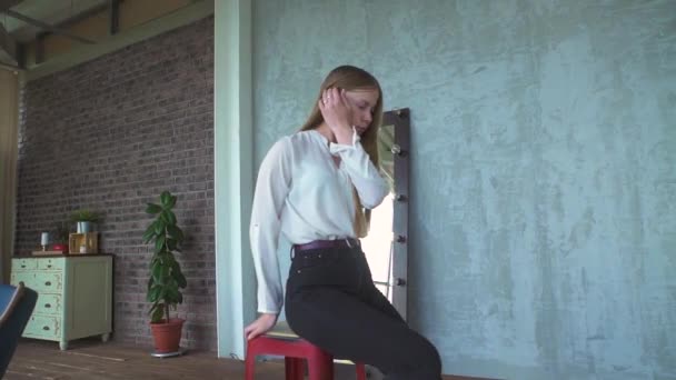 Beyaz bluzlu esmer kız stüdyoda kırmızı sandalyede oturan saçları düzeltiyor. — Stok video