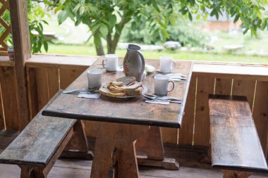 Kahverengi bir fincan kahve tarçın ve şeker ufuk yeşil ağaç ahşap banklar ile karşı doğal ahşap tablo.