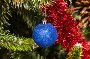 The christmas tree toy, blue ball or sphere on the fluffy artificial pine or fur branch ornament with red and blue garland 