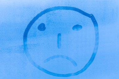 The picture or figure of the sad face on the blue evening or morning window glass with drops  clipart