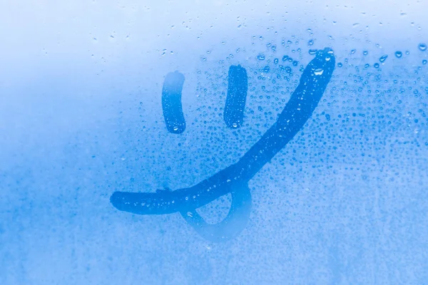 Mavi bir akşam ya da sabah camında damlaları olan gülen yüz resmi ya da figürü. 