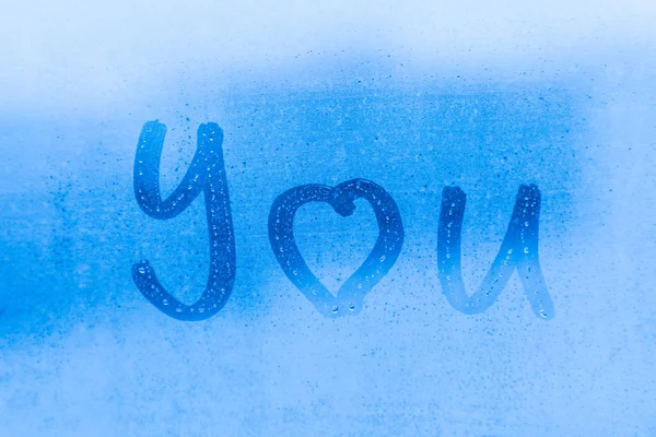 The romantic inscription I love you on the blue evening or morning window glass with drops