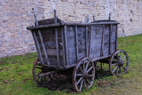 The broken ancient medieval rural wood cart or wagon on the green grass on the background of the castle or fortress stone or brick wall