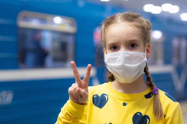 Mutlu ve mutlu bir çocuk sağlık merkezinde maskesini koruyor ya da koruyor ve sarı tişörtlü metroda ya da yeraltı koridorunda