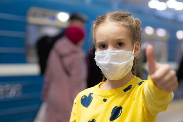 Mutlu ve mutlu bir çocuk sağlık merkezinde maskesini koruyor ya da koruyor ve sarı tişörtlü metroda ya da yeraltı koridorunda