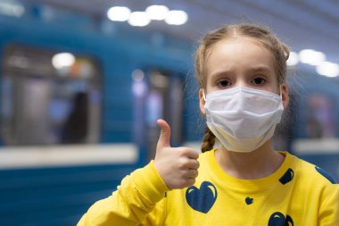 Glad and happy beautiful joy child in the medical helthcare guarding or protecting mask and in yellow t-shirt in the tube, subway or underground hall clipart
