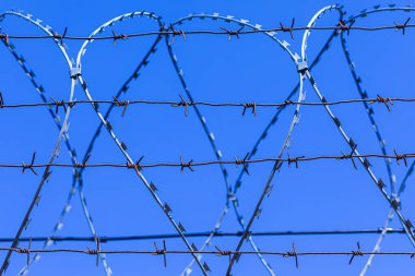 Mavi gökyüzünün arka planındaki dikenli tel silueti.