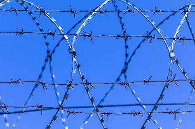 Mavi gökyüzünün arka planındaki dikenli tel silueti.