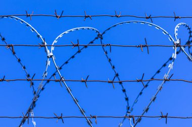 Mavi gökyüzünün arka planındaki dikenli tel silueti.