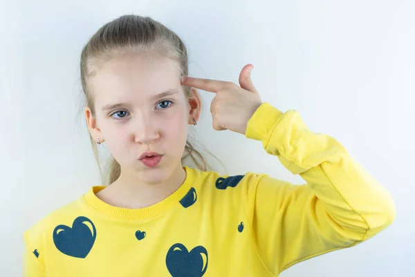 Sarı süveter giyen komik, havalı, güzel ve güzel bir kız ya da beyaz arka planda kolay çıkartma için tişört, işaret ya da zor durumun simgesi olarak şakağın yanında işaret parmağı