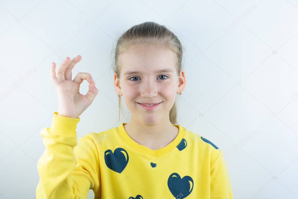 Vivid or colorful workpiece with funny, cool, pretty and nice girl in yellow sweater or tee-shirt on white background for easy extraction showing ok sign with her fingers