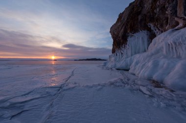 Buzlu su sıçramalarına şafak ışıklarıyla kayada kış Deniz Baykal, Kurminskiy Körfezi