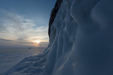 Buzlu su sıçramalarına (buz dışarı sıçrama) şafak ışıklarıyla kayada kış Deniz Baykal, Kurminskiy Körfezi