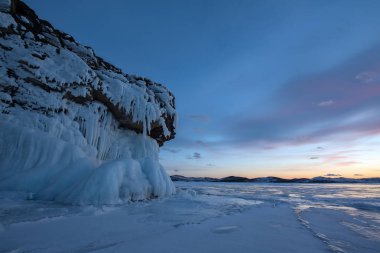 Buzlu su sıçramalarına (buz dışarı sıçrama) şafak ışıklarıyla kayada kış Deniz Baykal