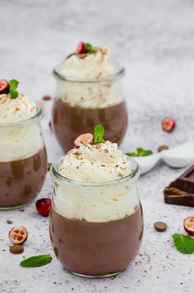 Chocolate cream on agar agar with whipped cream on top in glass jars on a light stone background.