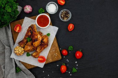 Kesme tahtasında kızarmış tavuk bacağı ve koyu arkaplanda acı biber sosu..