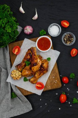 Kesme tahtasında kızarmış tavuk bacağı ve koyu arkaplanda acı biber sosu..