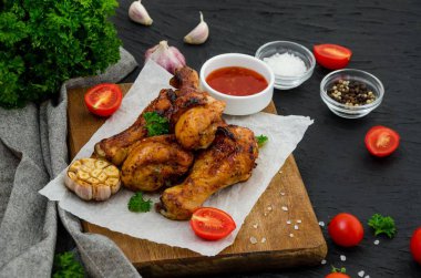 Kesme tahtasında kızarmış tavuk bacağı ve koyu arkaplanda acı biber sosu..