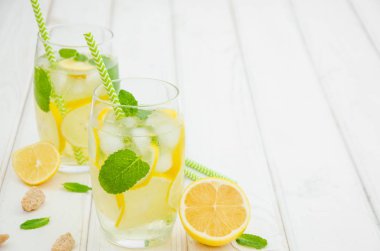 Limon dilimli ev yapımı limonata, beyaz ahşap arka planda buzlu bardakta nane ve esmer şeker..