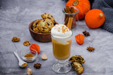 Baharatlı kremalı bir bardakta balkabaklı latte ve gri taşta çikolatalı kurabiyelerle birlikte tarçın çubuğu. Sonbahar içkisi. Şükran Günü içkisi.