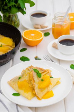 Portakal soslu krep ve beyaz ahşap arka planda bir fincan kahve. Lezzetli ve güzel kokulu kahvaltı..