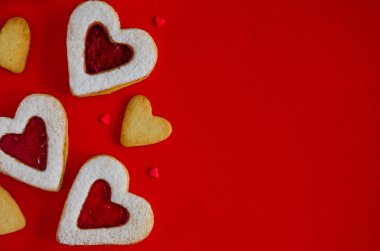 Sevgililer Günü yemek geçmişi. Kalp şeklinde Linzer kurabiyeleri, reçelli ve kırmızı arka planda krema şekeri. Sevgililer Günü için krem kartı. Boşluğu kopyala, üst görünüm.