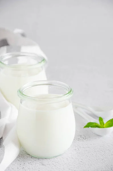 Homemade fresh organic yogurt in glass jars against a light background. Healthy food. Vertical orientation. Copy space.