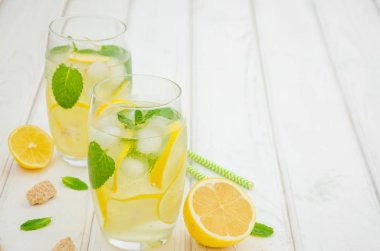 Limon dilimli ev yapımı limonata, beyaz ahşap arka planda buzlu bardakta nane ve esmer şeker. Yatay yönelim.