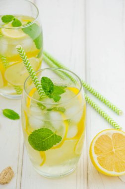Limon dilimli ev yapımı limonata, beyaz ahşap arka planda buzlu bardakta nane ve esmer şeker. Dikey yönelim.