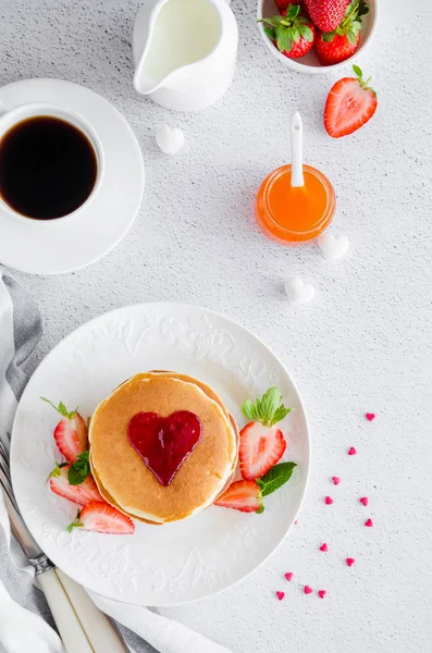 A stack of pancakes with a heart of jam on top with fresh strawberries and mint on a white plate on a light background. Breakfast for Valentine's Day. Vertical orientation. Copy space. Top view. — Stock Photo, Image