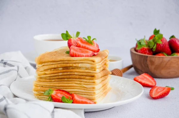 Crêpes, traditionelle russische Pfannkuchen auf einem weißen Teller mit frischen Erdbeeren und Honig auf hellem Hintergrund. Russisch masleniza. horizontale Orientierung. Nahaufnahme. — Stockfoto