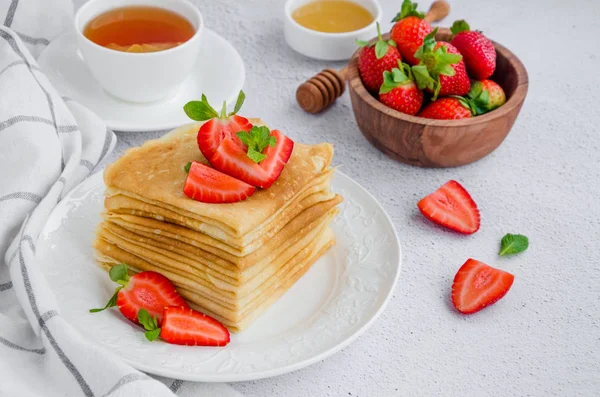 Crêpes, traditionelle russische Pfannkuchen auf einem weißen Teller mit frischen Erdbeeren und Honig auf hellem Hintergrund. Russisch masleniza. horizontale Orientierung. Nahaufnahme. — Stockfoto