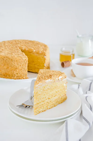 Du gâteau au miel. Gâteau russe traditionnel en couches Medovik avec crème sure sur une assiette blanche sur un fond blanc. Orientation verticale. Espace de copie — Photo