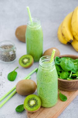 Fresh dietary green smoothies of spinach, banana, kiwi, yogurt and chia seeds in glass jars with straw on a gray background. Healthy eating. Vertical orientation. Copy space.