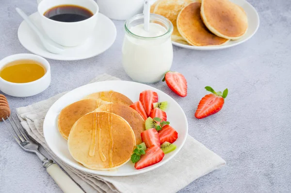 Traditionelle russische Pfannkuchen auf Kefir mit Honig, saurer Sahne, frischen Erdbeeren und Kiwi auf einem weißen Teller mit einer Tasse Kaffee. Gesundes Frühstück. Russische Masleniza. Horizontale Orientierung. — Stockfoto