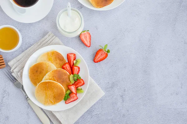 Traditionelle russische Pfannkuchen auf Kefir mit Honig, saurer Sahne, frischen Erdbeeren und Kiwi auf einem weißen Teller mit einer Tasse Kaffee. Gesundes Frühstück. Russische Masleniza. Ansicht von oben, Kopierraum — Stockfoto
