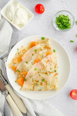 Geleneksel Rus ince krepleri, krem peynirli krepler, füme somon balığı ve açık arkaplanda yeşil soğan. Tatil Maslenitsa 'sı. Dikey oryantasyon. Üst görünüm.