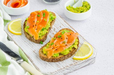 Avokado tostları. Çavdar ekmeği, avokado, füme somon, yeşil soğan ve susam tohumundan tost. Sağlıklı kahvaltı ya da öğle yemeği. Yatay oryantasyon. Kapat.