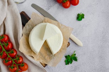 Ev yapımı yumuşak peynir brynza ya da ahşap kesim tahtasındaki peynirli maydanoz ve gri arka planda vişneli domates. Yatay yönelim, üst görünüm, kopyalama alanı