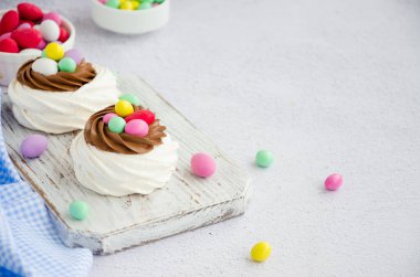 Mini Pavlova Kuş Yuvası çikolata kremalı ve renkli şekerli açık arkaplanlı. Merengue Kurabiyeleri. Çocuklar için yemek fikri. Paskalya pastası. Yatay oryantasyon. Boşluğu kopyala
