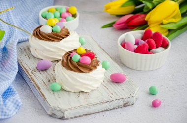 Mini Pavlova Kuş Yuvası çikolata kremalı ve renkli şekerli açık arkaplanlı. Merengue Kurabiyeleri. Çocuklar için yemek fikri. Paskalya pastası. Yatay yönelim