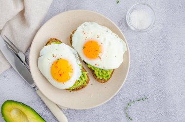 Avokado tostu, kızarmış yumurta ve gri bir zeminde deniz tuzu. Sağlıklı bir kahvaltı ya da öğle yemeği. Yatay yönelim