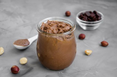 Koyu arkaplanda cam bir kavanozda ev yapımı çıtır çikolatalı fındık ezmesi. Yatay yönelim