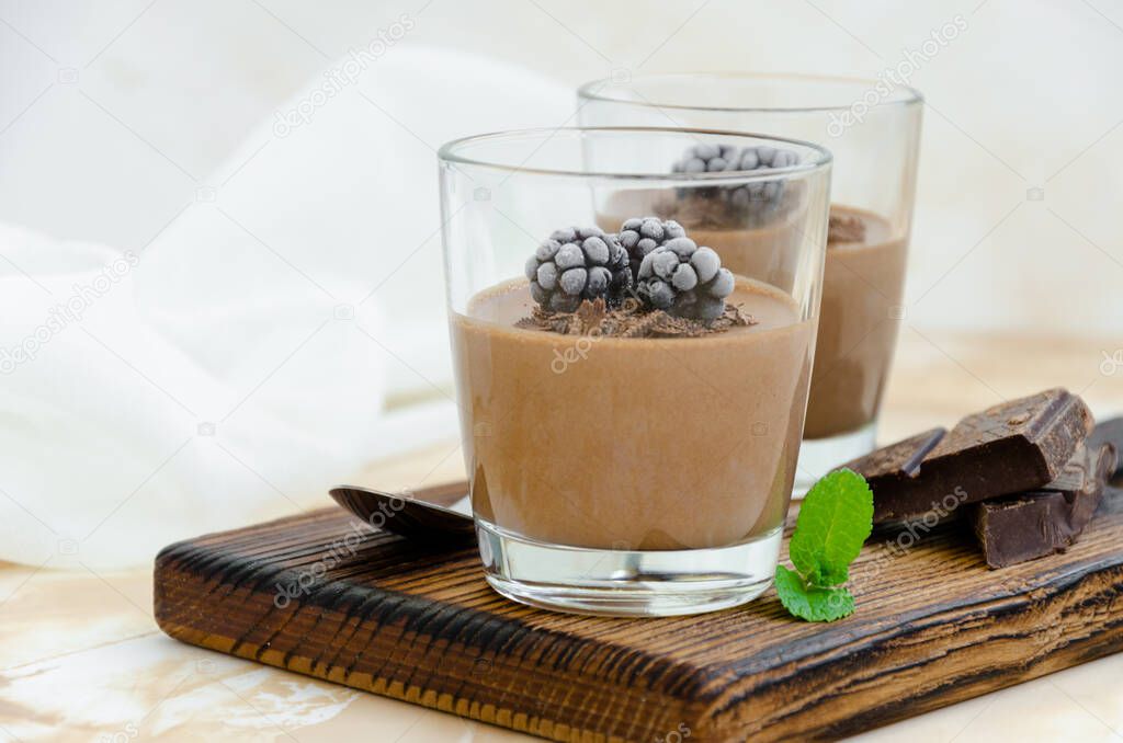 Italian dessert - chocolate panna cotta, mousse, cream or pudding with blackberry in a glass on a board on a light concrete background. Horizontal orientation. Copy space.