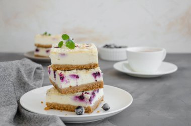 Siyah frenk üzümlü cheesecake ve beyaz bir tabakta çırılçıplak, koyu beton arka planda bir fincan çay. Frenk üzümlü kek. Lezzetli tatlı. Yatay oryantasyon. Boşluğu kopyala